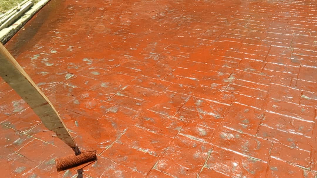 Terracotta-red stamped concrete surface being sealed with a roller